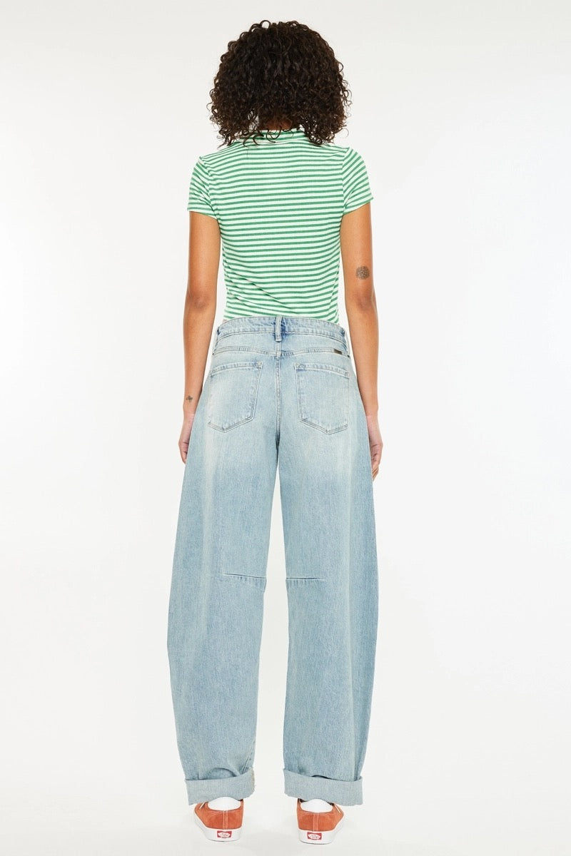A model shown from the back wearing a green and white striped short-sleeve top, light-wash wide-leg denim jeans, and brown platform sandals, set against a plain white studio background.