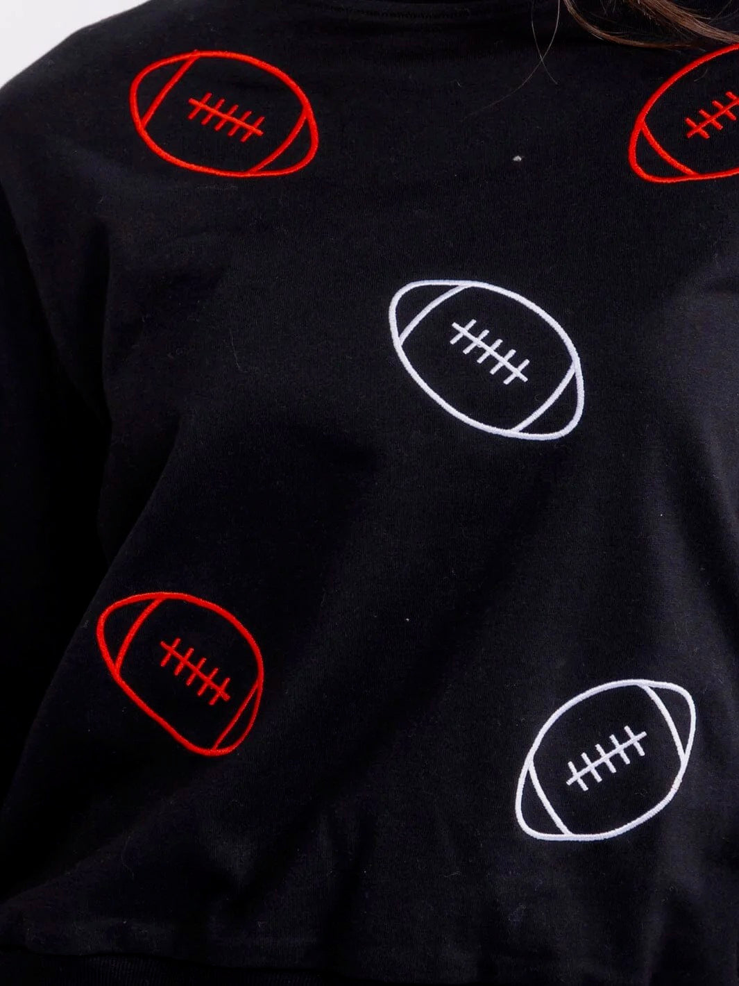 A close-up of a black sweatshirt featuring an all-over pattern of embroidered American footballs in red and white.