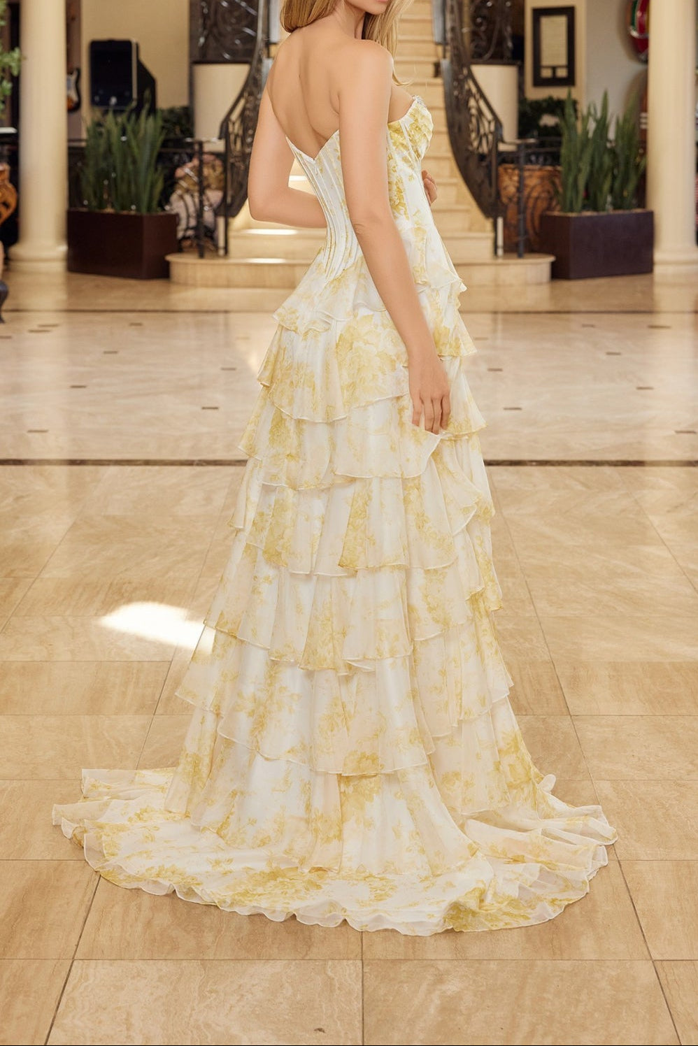 Woman in a floral dress standing in an elegant indoor setting with a chandelier.