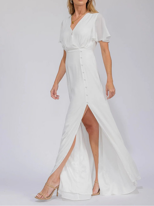 Woman wearing a white evening gown with a slit on a plain background