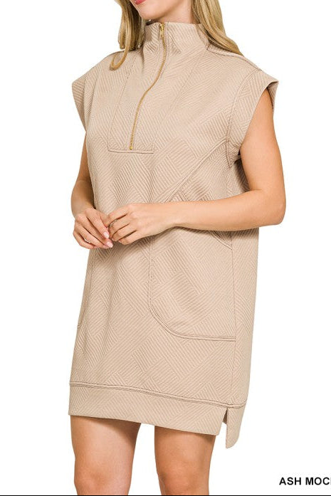 A woman modeling a sleeveless, high-neck, half-zip mini dress in a light ash mocha color, shown against a plain white background.