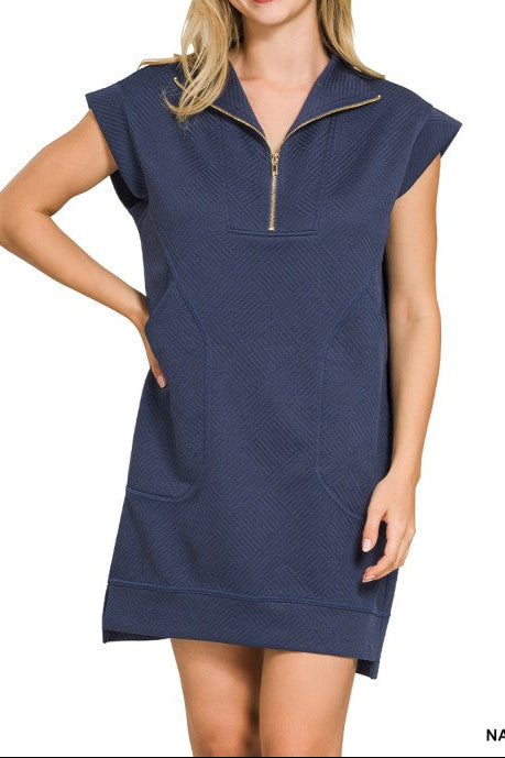 A woman modeling a navy blue short-sleeve quarter-zip pullover dress with a textured knit fabric and side pockets, shown against a plain white background.