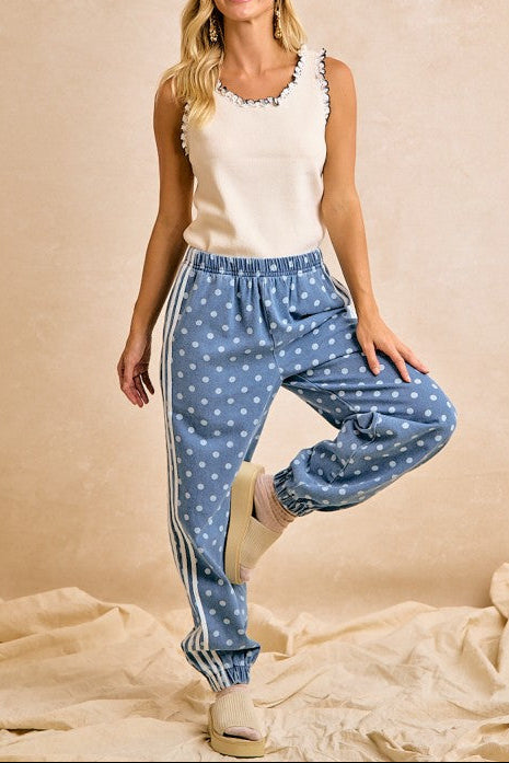 Woman wearing a white sleeveless top and blue polka dot pants on a beige background