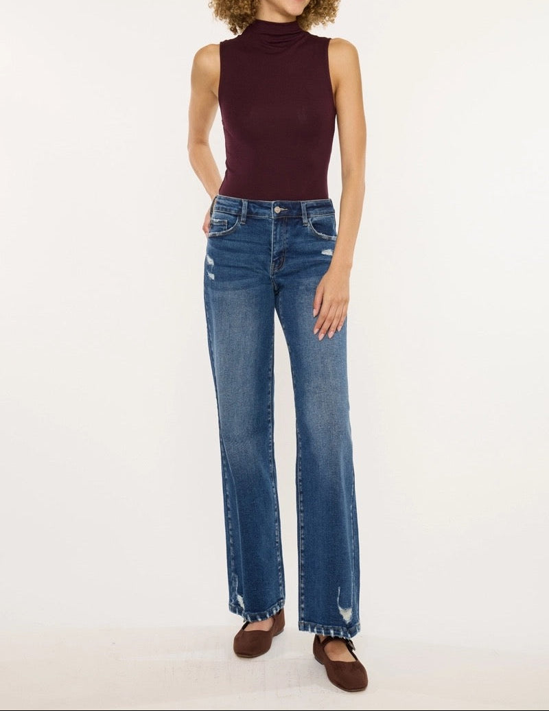 Woman wearing a sleeveless burgundy top and blue jeans on a white background
