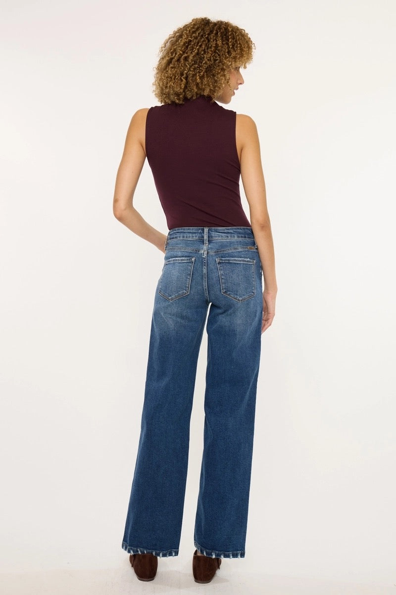 A woman shown from the back wearing a sleeveless dark burgundy top and high-waisted, wide-leg blue jeans against a plain white studio background.
