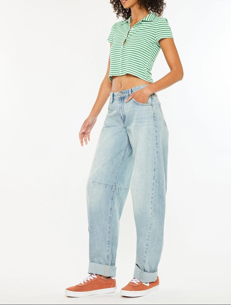 A model wearing a green and white striped short-sleeve crop top, light-wash wide-leg denim jeans, and orange sneakers, standing against a plain white studio background.