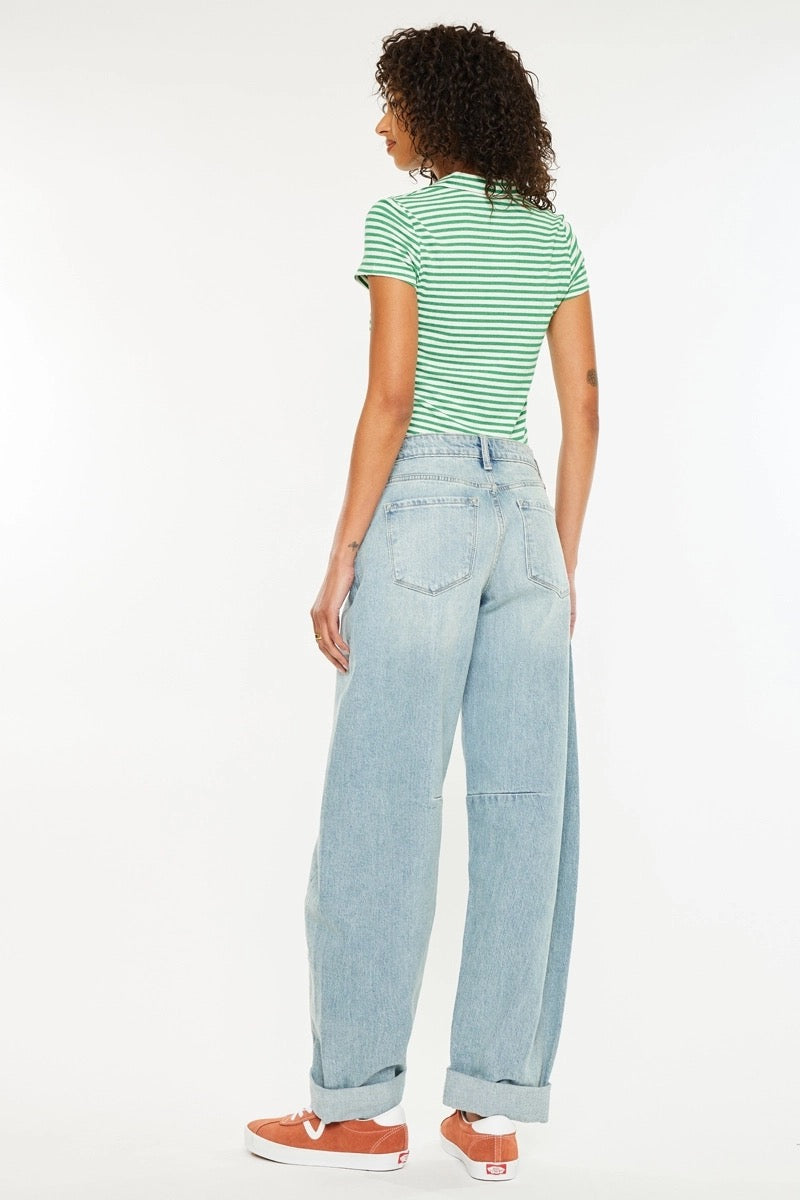 A woman shown from the back wearing a green and white striped short-sleeve top, light-wash wide-leg denim jeans, and orange sneakers against a plain white studio background.