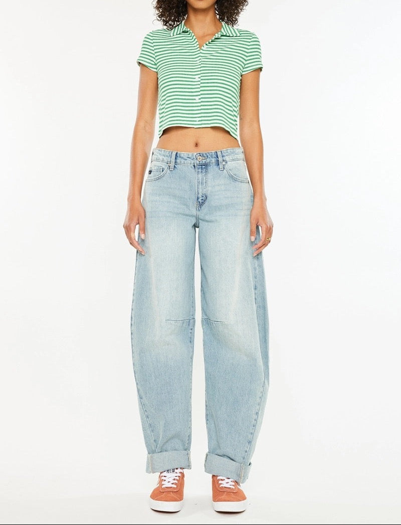 A model stands against a white studio background wearing a green and white striped short-sleeve crop top, light-wash wide-leg jeans, and orange sneakers.