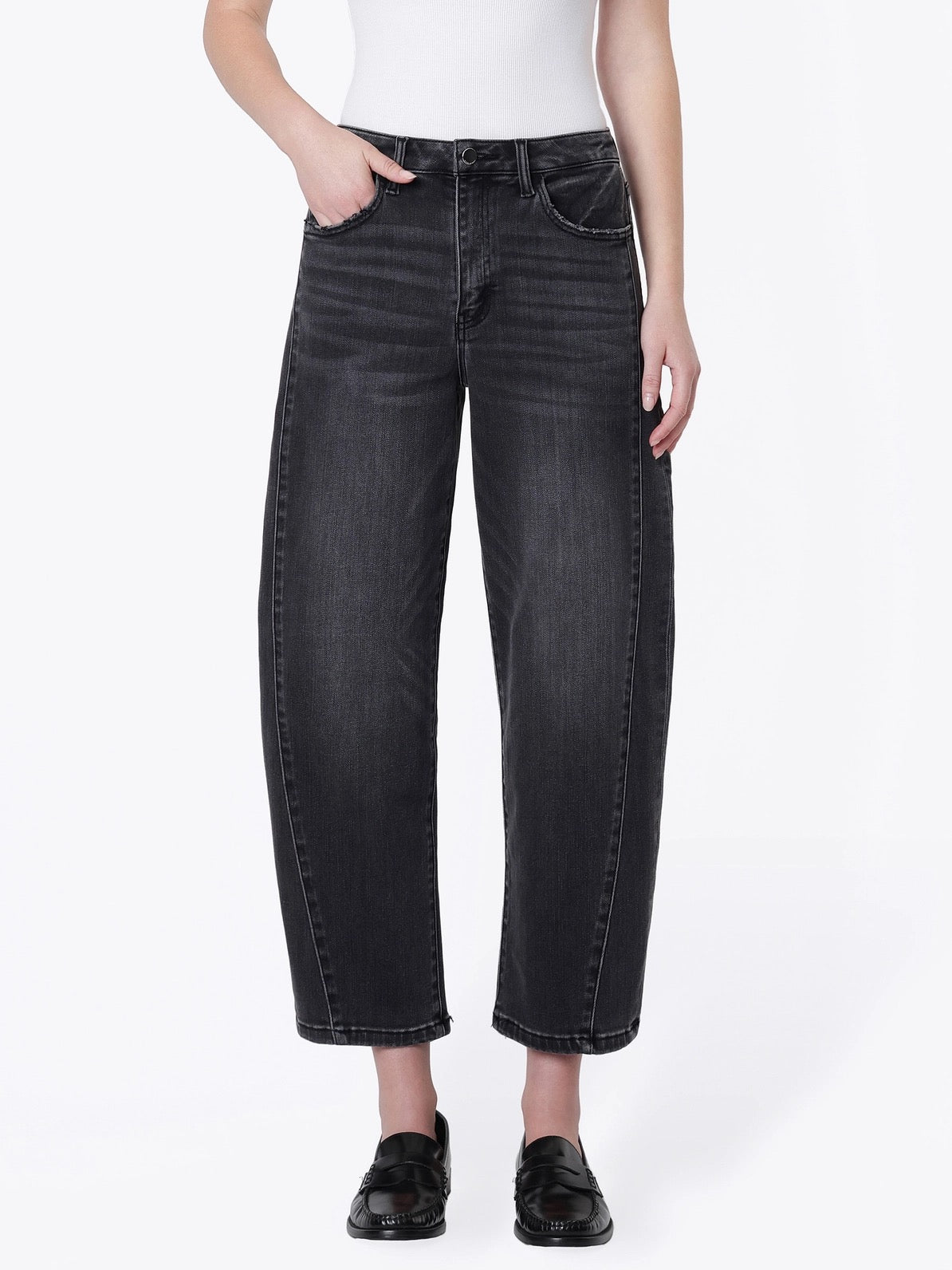 A model wearing a pair of wide-leg cropped jeans in a washed black denim, paired with a white top and black loafers, against a plain white studio background.