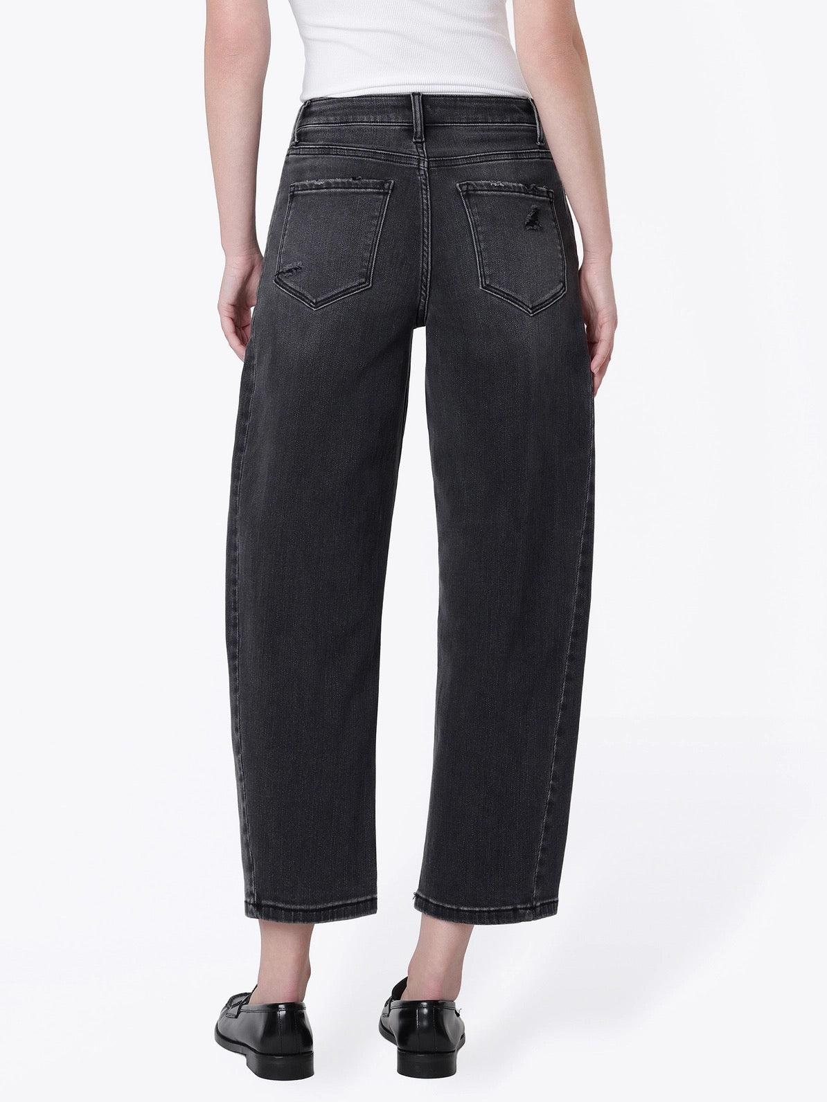 Rear view of a model wearing dark gray wide-leg cropped jeans with a white top and black shoes, against a plain white studio background.