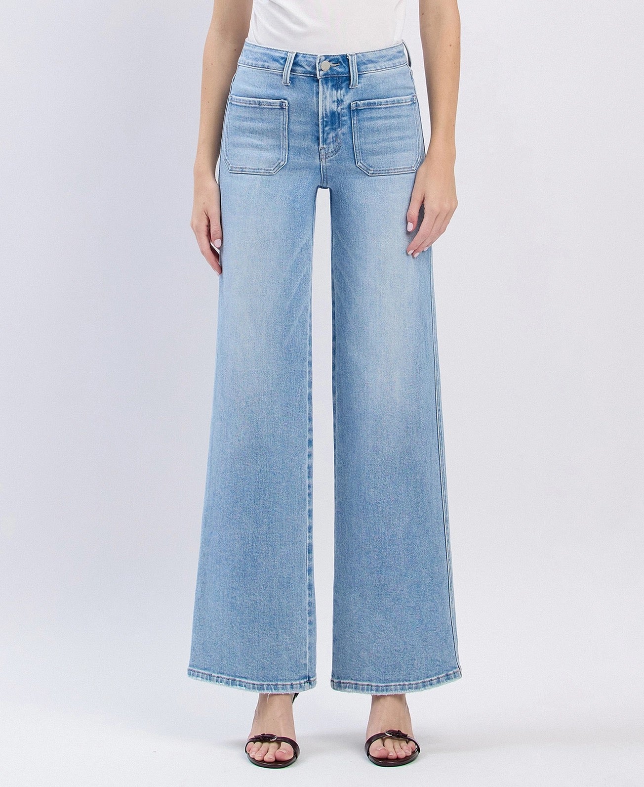 A model wearing light blue wide-leg denim jeans with a faded wash, paired with a white top and black sandals, shown against a light gray studio background.