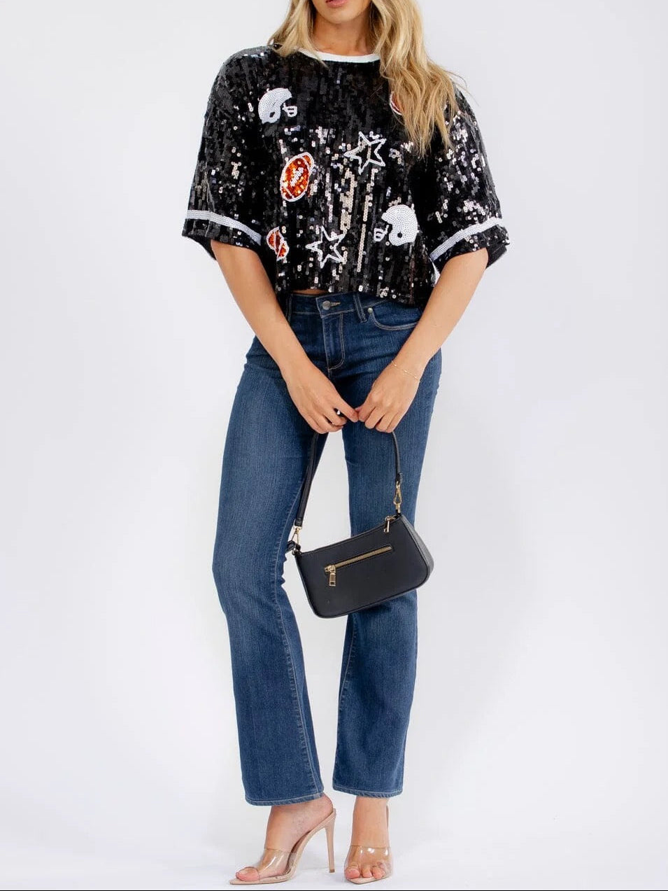 Woman wearing a black sequin top and blue jeans, holding a black handbag on a white background