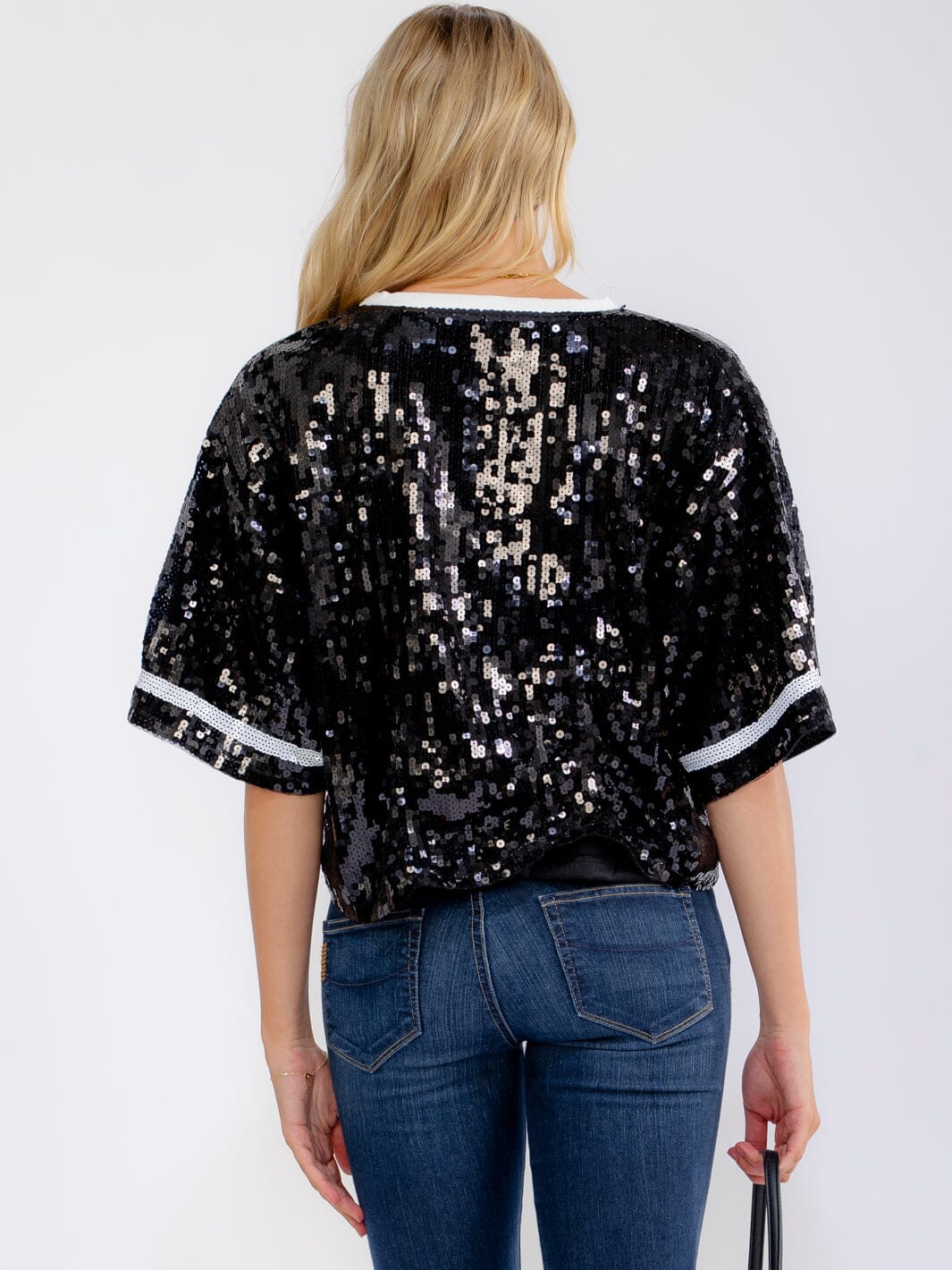 Person wearing a black sequin top and blue jeans on a white background