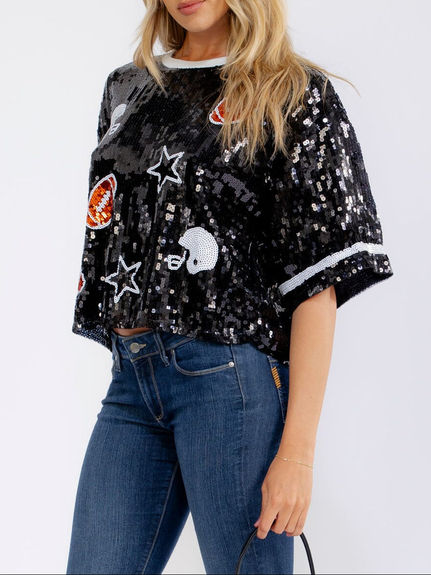 Woman wearing a black sequin bomber jacket with various patches on a white background