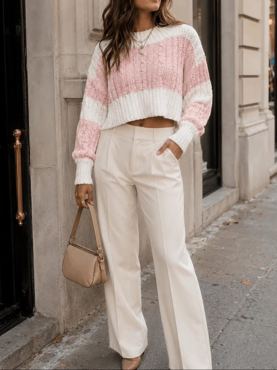 Woman wearing a pink and white striped sweater and white pants, standing on a city street.