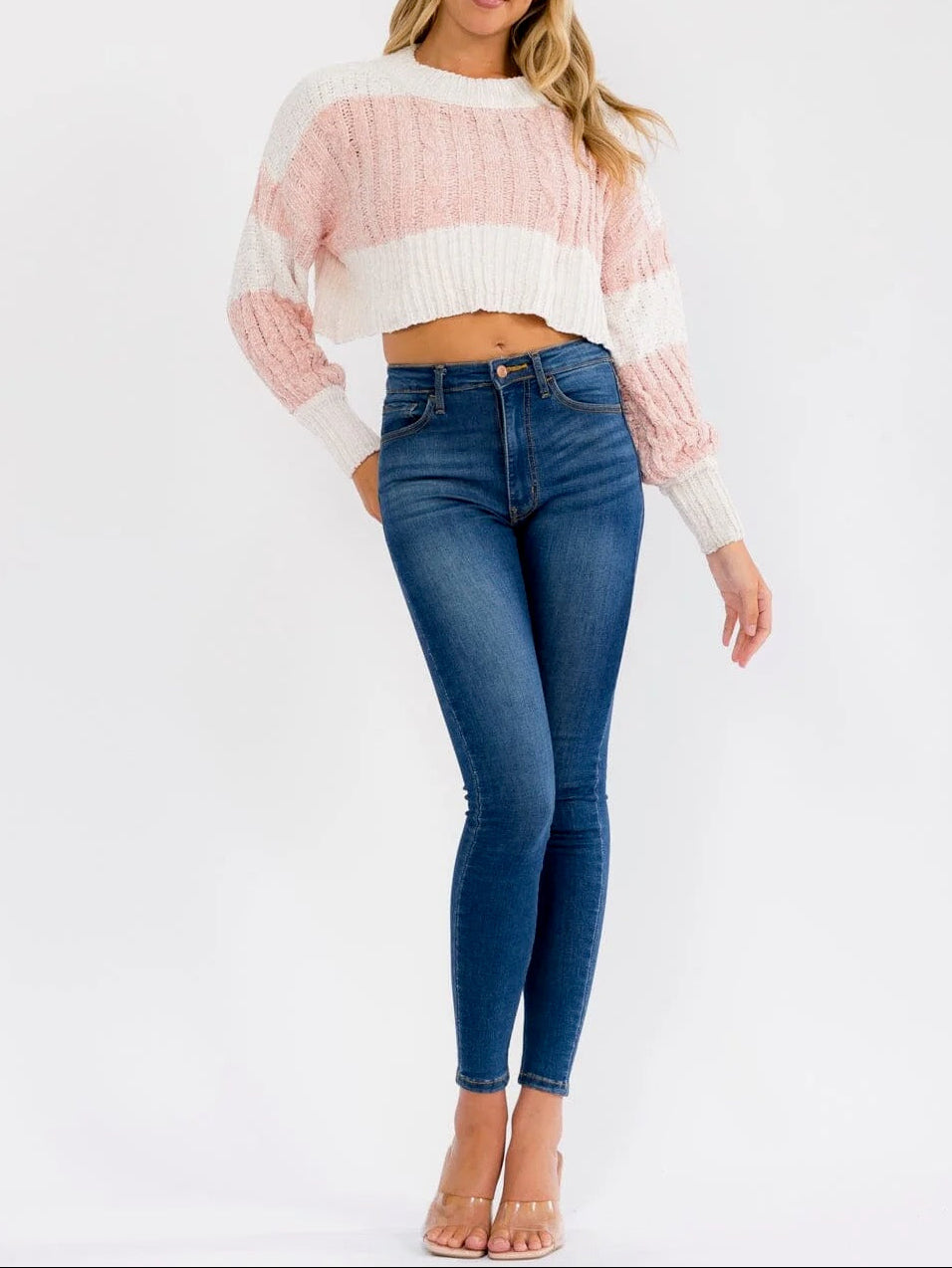 Woman wearing a pink and white sweater and blue jeans on a white background