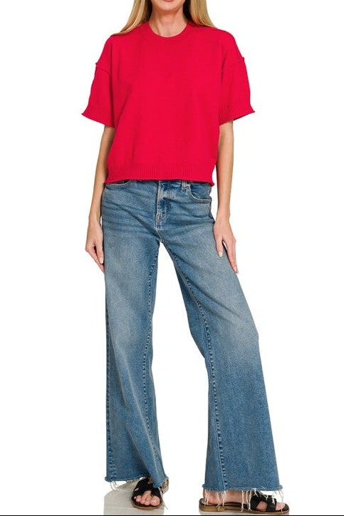 A woman modeling a bright red short-sleeve crop top and wide-leg blue jeans against a plain white background.