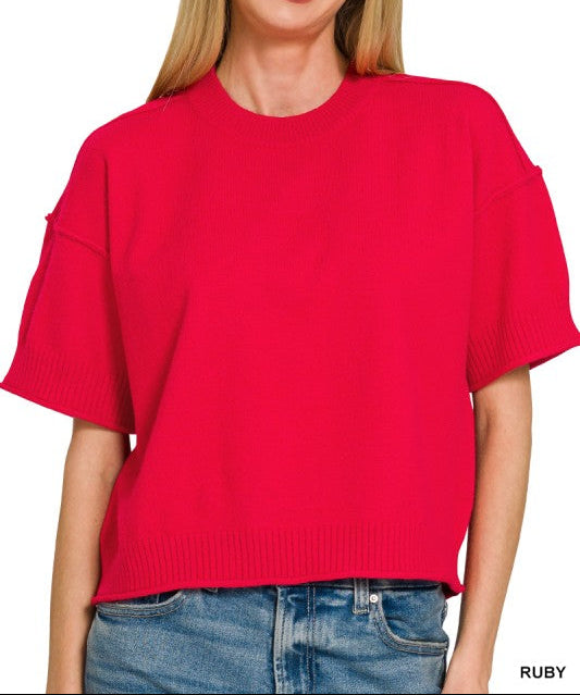 A woman wearing a bright red short-sleeve knit top with a crew neck and slightly cropped, wide sleeves, paired with blue jeans against a plain white background.